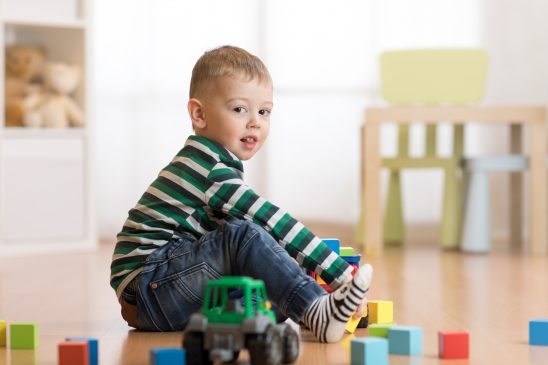 Lovely toddler boy playing with building cubes in kindergarten, siting on floor